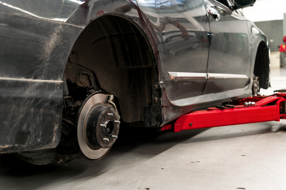 Épave de voiture sans roue, posée sur un cric hydraulique dans un atelier